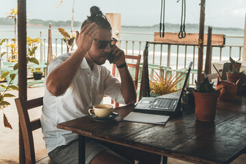 Mężczyzna, cyfrowy nomada pracujący z laptopem i telefonem przy stoliku w kawiarni, praca zdalna...