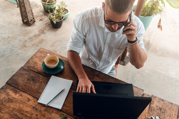 Mężczyzna, cyfrowy nomada pracujący z laptopem i telefonem przy stoliku w kawiarni, praca zdalna...