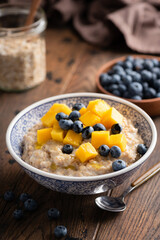 Oatmeal bowl with blueberries and mango on wooden table, healthy breakfast food