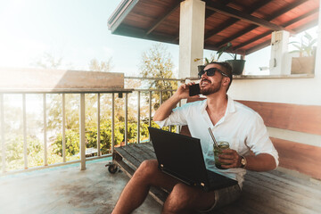 Mężczyzna, cyfrowy nomada pracujący z laptopem i rozmawiający przez telefon komórkowy w słoneczny dzień. - obrazy, fototapety, plakaty