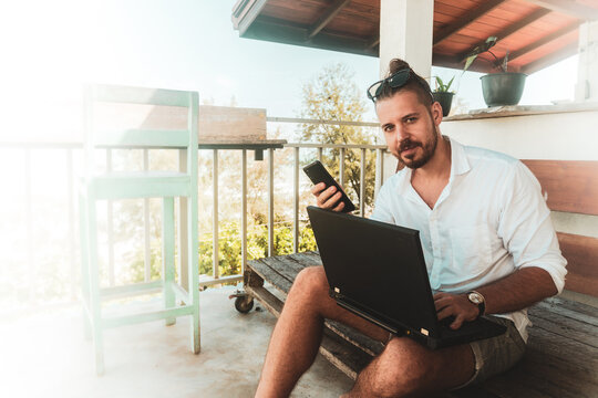 Mężczyzna, cyfrowy nomada pracujący z laptopem i rozmawiający przez telefon kom&oacute;rkowy w słoneczny dzień.