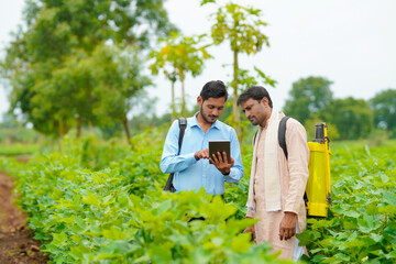 Young indian agronomist showing some information to farmer in tablet at agriculture field. - obrazy, fototapety, plakaty