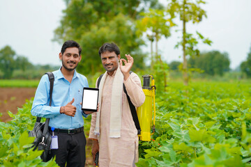 Young indian agronomist or banker showing tablet with farmer at agriculture field.