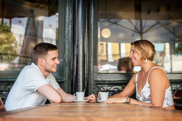 A blonde girl and a boy drinking coffee in an outdoor cafeteria sharing laughter and knowing glances
