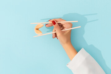 Female hand holding fortune cookie with chinese chopsticks over blue background