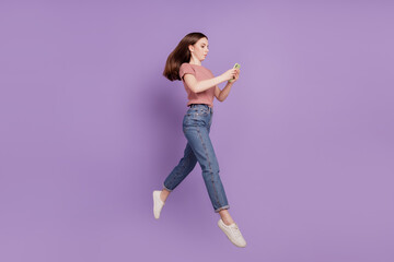 Photo of cheerful girl jumping going in air using cellphone isolated over violet background