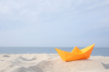 Orange paper boat on sandy beach near sea, space for text