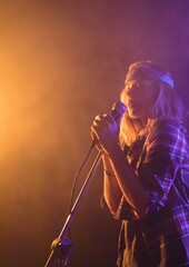 Caucasian female musician singing on a microphone at music concert