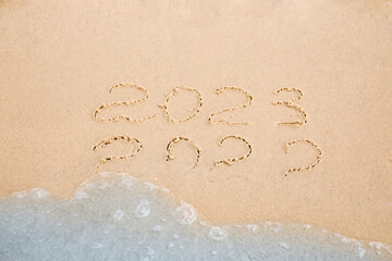 Dates written on sandy beach. 2022 washed by sea wave as New 2023 Year coming