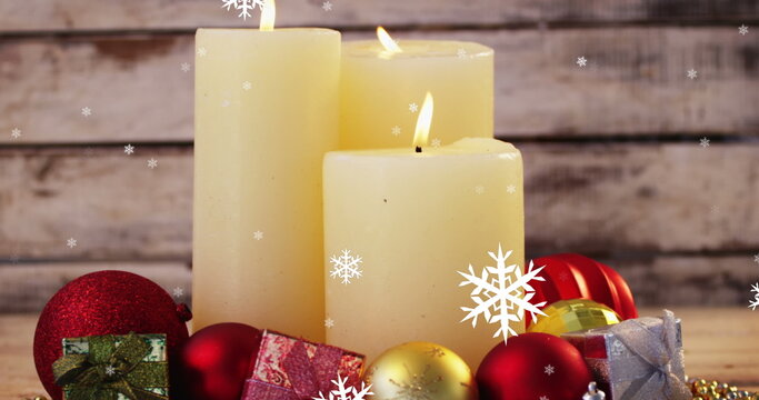 Image of three lit candles, snowflakes falling over wooden surface