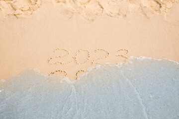 Dates written on sandy beach. 2022 washed by sea wave as New 2023 Year coming