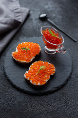 Red caviar in a bowl and caviar sandwiches on a black stone board