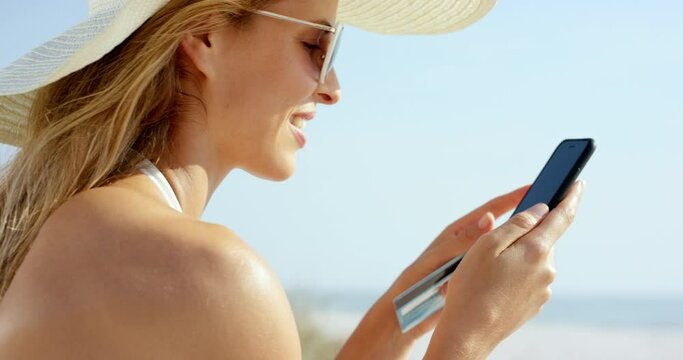 Woman using credit card shopping online with mobile phone at the beach on vacation