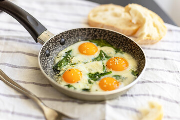 Selective focus to fried eggs with spinach, cheese and hemp seeds in skillet. Healthy breakfast or brunch.