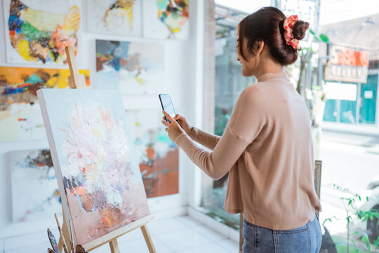 asian female artist taking picture of her own painting using smartphone