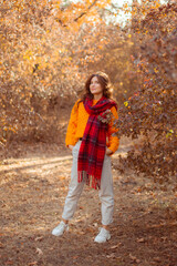 a young woman in an orange sweater wraps herself in a scarf in an autumn park