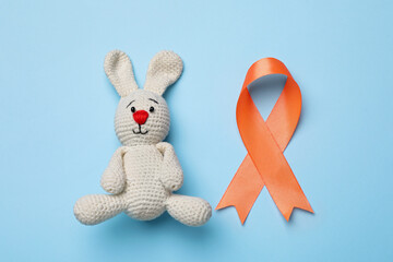 Orange ribbon and toy bunny on light blue background, flat lay. Multiple sclerosis awareness