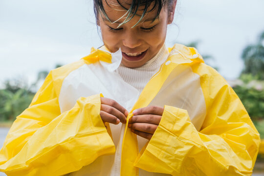 Crop smiling Asian girl buttoning up raincoat in park