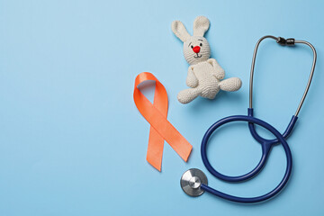 Orange ribbon, toy bunny and stethoscope on light blue background, flat lay with space for text....