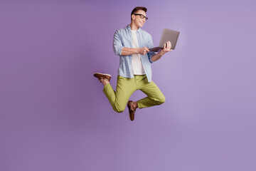 Portrait of programmer guy jump hold laptop typing working on violet background