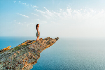 A young woman stands on a picturesque steep cliff above the sea against the sky. The concept of...