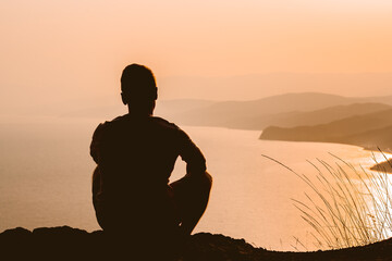 Silhouette of a man at sunset on a cliff with a magnificent landscape and a view of the sea and mountains