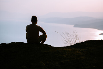 Silhouette of a man at blue sunrise on a cliff with a magnificent landscape and a view of the sea and mountains