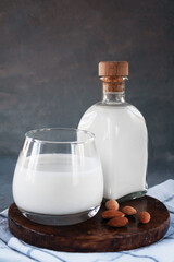 Glass and bottle of almond milk on gray background with almonds