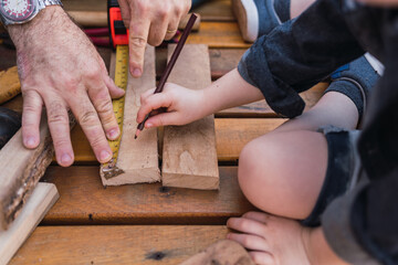 Crop father with son measuring wooden plank