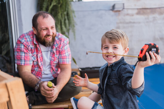 Cheerful boy playing with tape measure against father
