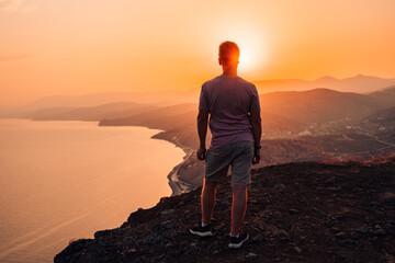 A young man stands on the edge of a cliff at sunset with an incredible view of the mountains