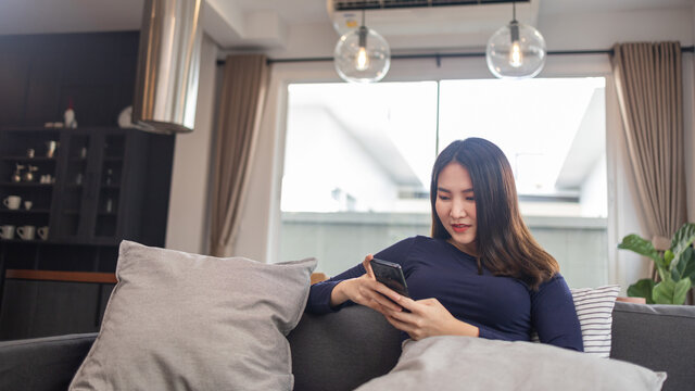 Work from home concept a young businesswoman sitting on a cozy sofa using her mobile phone chatting with the customers