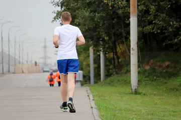 Man in shorts running on sidewalk along the city street, rear view. Runner in city, workout in autumn season