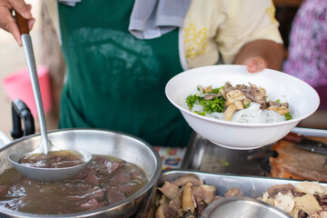 The cook is scooping the soup from the pot into the bowl.