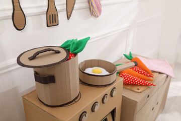 Fototapeta na wymiar Toy cardboard kitchen with stove and utensils indoors