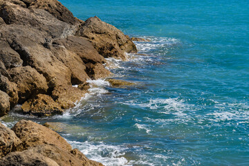 Obraz premium Waves of the Mediterranean Sea on a rocky coast in Cyprus near the city of Paphos in sunny summer weather. Crystal clear emerald water and rocky coastline of the Mediterranean Sea, Cyprus