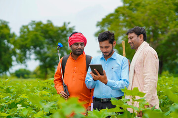 Young indian agronomist or banker showing some information to farmer in tablet at agriculture field.