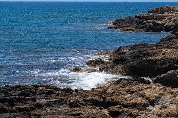 Fototapeta na wymiar Sea surf, blue waves of Mediterranean sea in the Cyprus. Rocky stoned beach. Summer day. Sunny paradise. Sunny daytime seascape. View on the beach of Cyprus. Stones near mediterranean sea
