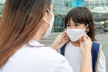 Asian mother helps her daughter wearing a medical mask for protection Covid-19 or coronavirus outbreak prepare to go to school when back to school order.