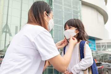 Asian mother helps her daughter wearing a medical mask for protection Covid-19 or coronavirus outbreak prepare to go to school when back to school order.
