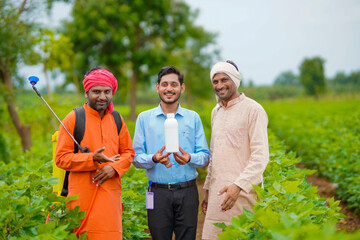 Young indian agronomist giving liquid fertilizer bottle to farmer.