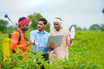 Young indian agronomist giving liquid fertilizer bottle to farmer and showing product information...