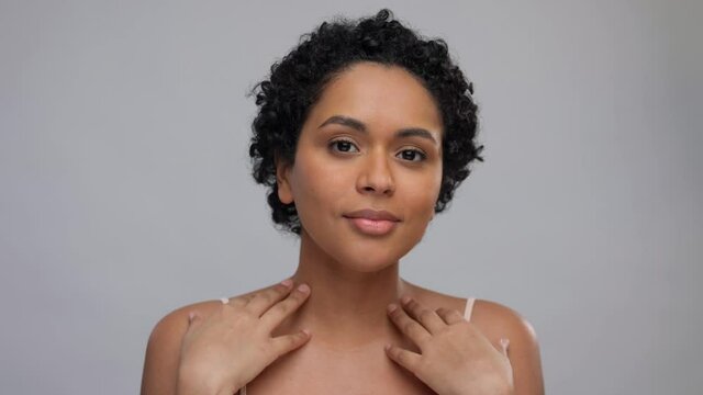 beauty and people concept - portrait of happy smiling young african american woman with bare shoulders touching her face over grey background