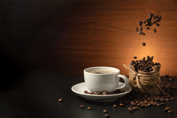 falling coffee beans on burlap bag andcoffee cup on dark background
