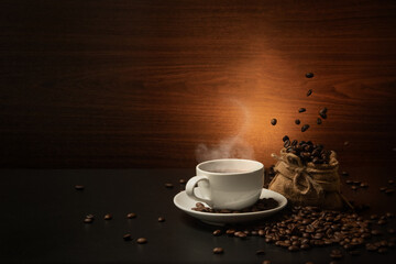 dropping coffee beans on burlap bag andcoffee cup on dark background