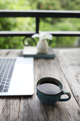 Espresso coffee cup and laptop side view on wooden table at the balcony