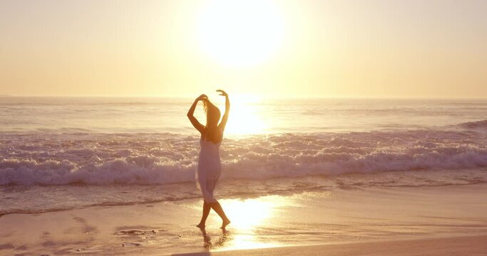Free happy woman with arms outstretched enjoying nature walking along beach at sunset face raised towards sky