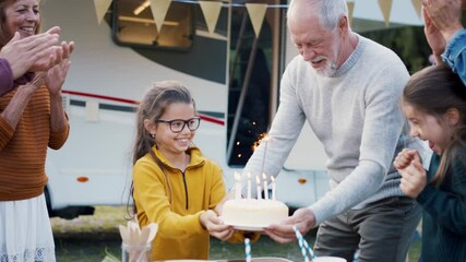 Multi-generation family celebrating birthday outdoors at campsite, caravan holiday trip.