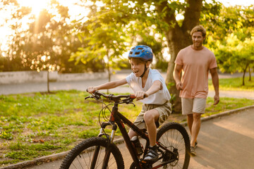 Ginger white man teaching his son how to ride bicycle in park