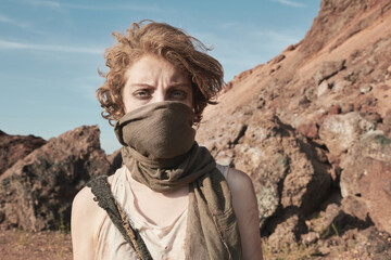 Portrait of young woman covering her face with scarf and looking at camera while standing in the desert